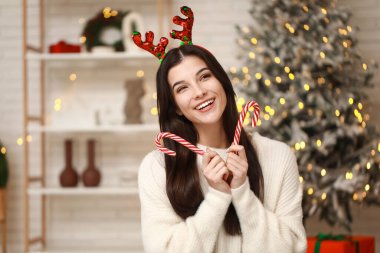 Noel arifesinde evde elinde baston şekerlerle ren geyiği boynuzlarıyla güzel genç bir kadın.