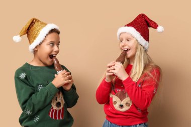 Küçük şirin çocuklar kahverengi arka planda çikolatalı Noel Baba yiyorlar.