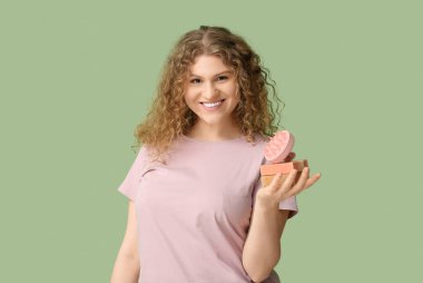 Saç derisi masaj aleti ve yeşil arka planda şampuan çubukları olan güzel bir genç kadın.