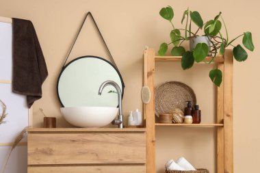 Lavabosu, çekmecesi ve bej duvarın yanında raf ünitesi olan hafif bir banyo.