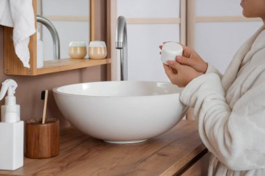 Genç bir kadın banyoda kozmetik ürünler kavanozunu tutuyor.