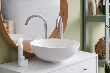 Modern lavabo, kavanoz ve kozmetik ürünleri banyodaki yeşil duvarın yanındaki çekmecelerde.