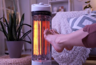 Akşamları elektrikli ısıtıcının yanında bacaklarını ısıtan genç bir kadın.