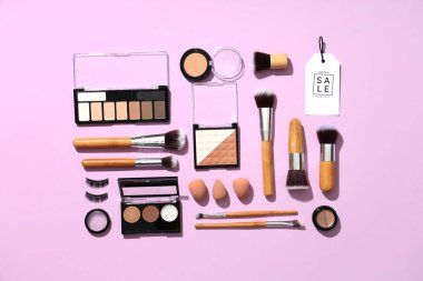 Dekoratif kozmetik ürünleri, makyaj fırçaları, süngerler ve renk arkaplanındaki satış etiketleriyle kompozisyon