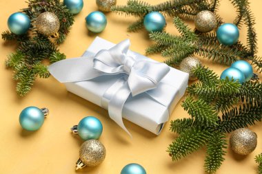 Topları ve sarı arka planda hediye kutusu olan Noel ağacı dalları