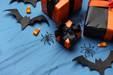 Hediye kutularıyla kompozisyon, lezzetli mısır şekerlemeleri ve Cadılar Bayramı için kağıt yarasalar mavi arka planda, yakın plan