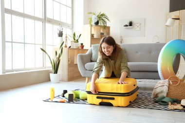 Evinde bavullu ve plaj aksesuarlı genç bir kadın var.