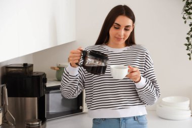Genç bir kadın mutfakta fincana kahve dolduruyor.