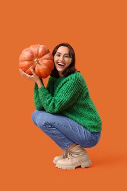 Turuncu arka planda balkabağı olan genç bir kadın.
