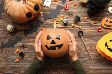 Ahşap masada boyalı Cadılar Bayramı kabağı taşıyan kadın.