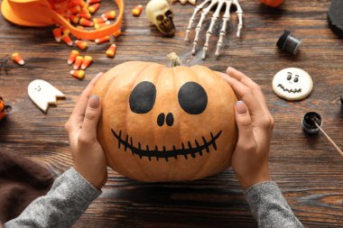 Ahşap masada boyalı Cadılar Bayramı kabağı taşıyan kadın.