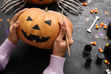 Cadılar Bayramı balkabağını siyah grunge masasında boyayan kadın.