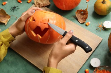 Yeşil grunge masasında Cadılar Bayramı balkabağı oyan kadın.