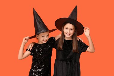 Cadılar Bayramı için turuncu arka planda cadılar gibi giyinmiş şirin küçük kızlar.