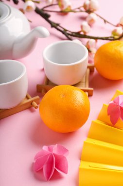 Fincanlı çaydanlık, mandalina ve pembe arka planda sakura. Japon Yeni Yıl Kutlaması