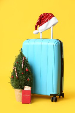 Noel Baba şapkalı bavul, Noel ağacı ve sarı arka planda pasaport.