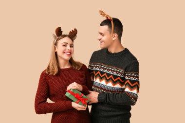 Geyik boynuzları takmış, bej arka planda Noel hediyesi kutusu olan güzel bir çift.