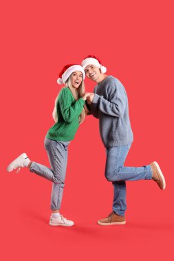 Kırmızı arka planda Noel Baba şapkalı mutlu çift