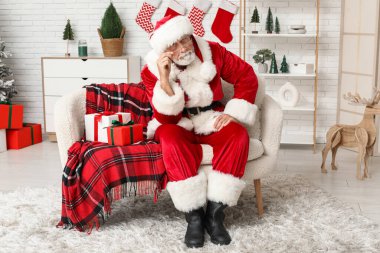 Noel Baba hediye kutularıyla Noel 'i evde koltukta kutluyor.