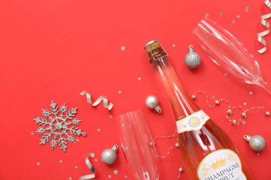 Kırmızı arka planda Noel dekoru olan şampanya şişesi ve bardaklar.