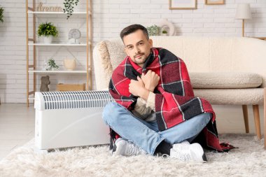 Evinde radyatör yakınında ekose ısıtıcısı olan hasta genç bir adam.