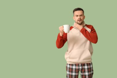 Yeşil arka planda bir fincan çayla hasta genç bir adam.