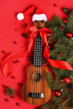 Ukulele ile kompozisyon, köknar dalları ve kırmızı arka planda Noel süslemeleri