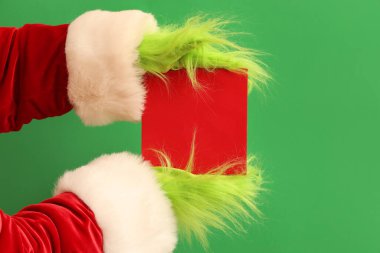 Yeşil saçlı Noel Baba kostümlü yaratık elleri ve yeşil arka planda boş bir kart.