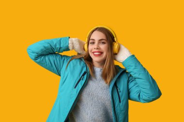 Sarı arka planda kulaklıkları olan sıcak kış kıyafetleri içinde güzel, genç bir kadın.