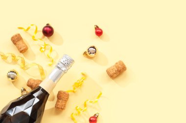 Mantarlı bir şişe şampanya ve sarı arka planda Noel topları.