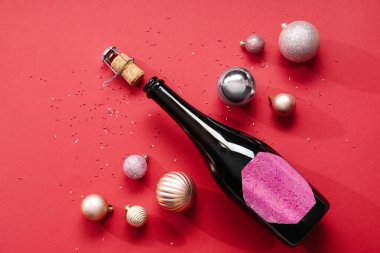 Bir şişe mantarlı şampanya ve kırmızı arka planda Noel topları.