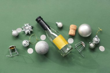 Bir şişe mantarlı şampanya ve yeşil arka planda Noel topları.