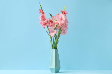 Mavi arka planda bir buket güzel gladiolus çiçeği olan vazo.