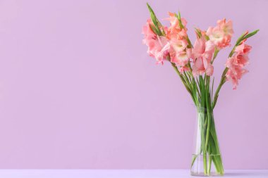 Leylak arka planında bir buket güzel gladiolus çiçeği olan cam vazo.