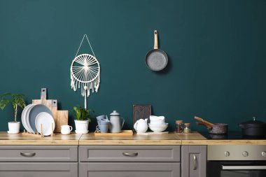 Mutfaktaki yeşil duvarın yanındaki tezgahlarda bitkiler olan temiz tabaklar.