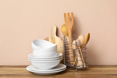 Bej duvarın yanındaki masada mutfak aletleri olan beyaz tabaklar.