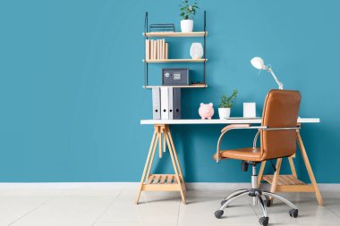 Modern kasa rafı, ev ofisinin mavi duvarında kitaplar ve bitkiler asılı.