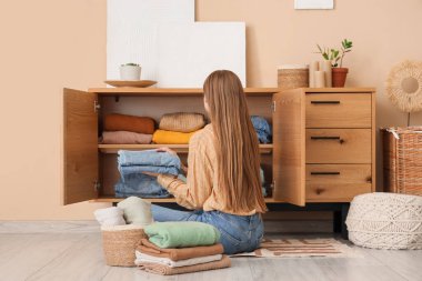 Güzel genç bir kadın, temiz giysileri evdeki dolabına koyuyor.