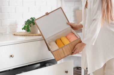 Katlanmış giysilerle sepeti evdeki çekmeceye koyan genç bir kadın.