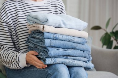 Bir yığın şık elbisesi olan genç bir kadın evdeki kanepede oturuyor.