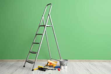 Yeşil duvarın yanında boya ve aletlerle dolu merdiven.