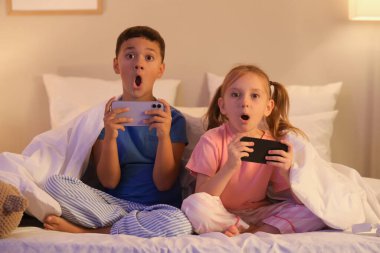 Cep telefonlu şirin çocuklar akşamları evde video oyunu oynuyorlar.