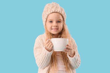 Mavi arka planda bir fincan kakaolu, kışlık elbiseli şirin küçük kız.