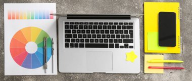 Çizgi dizüstü bilgisayarı, renk çizelgeleri, kırtasiyesi ve telefonu olan grafik tasarımcısının çalışma yeri, en üst görünüm