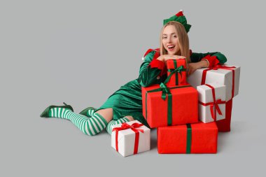 Beyaz arka planda Noel hediyesi kutuları olan elf kostümlü genç bir kadın.