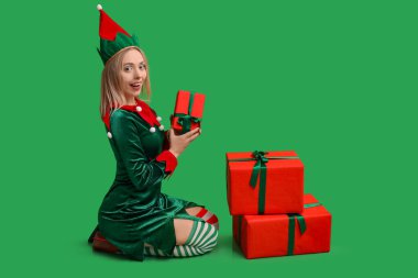 Yeşil arka planda Noel hediyesi kutuları olan elf kostümlü güzel bir genç kadın.