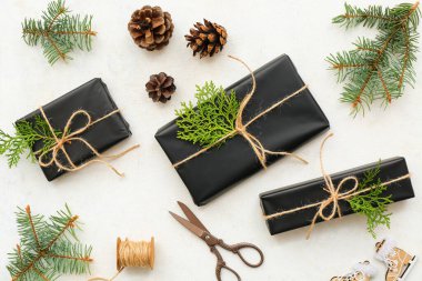 Beyaz arka planda Noel ağacı dalları ve konileri olan siyah hediye kutuları