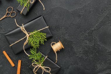 Noel hediye kutularında kozalaklı dallar ve siyah arka planda tarçın var.