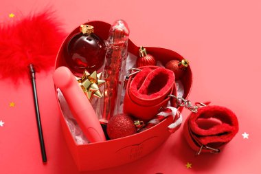 Farklı seks oyuncakları ve kırmızı arka planda Noel dekoru olan kalp şeklinde bir kutu.