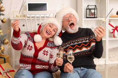 Evde şampanya içen, yılbaşı maytaplı olgun bir çift.